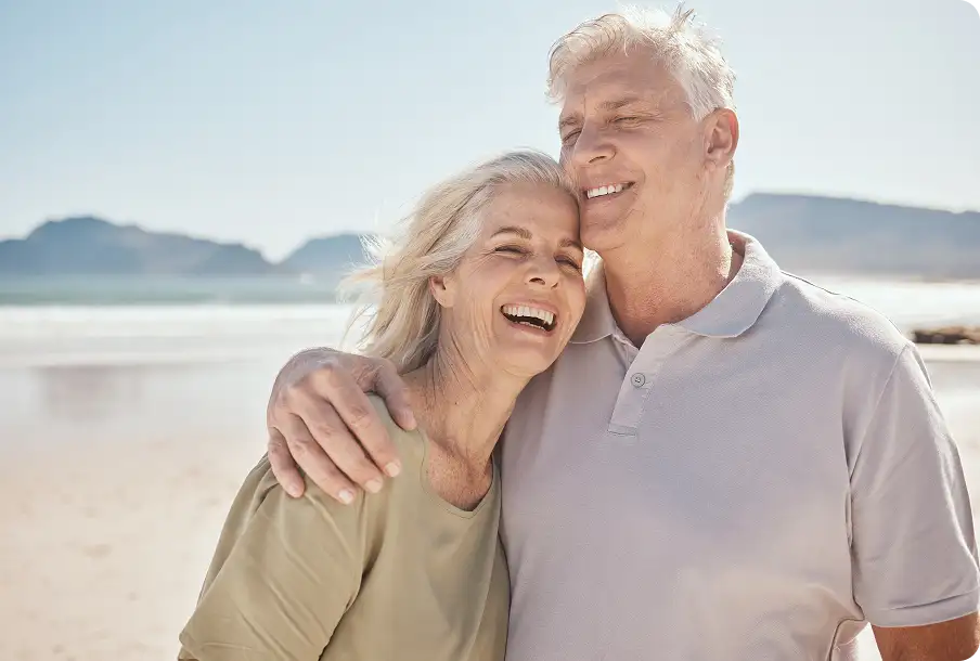 Elderly couple hugging on sunset beach – romance with restored IOLs vision.